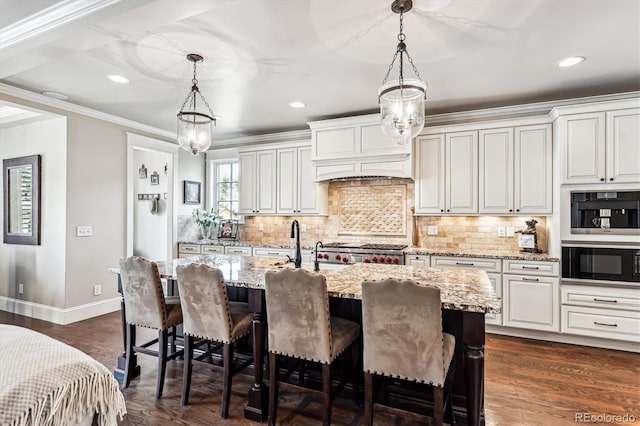 kitchen featuring light stone counters, decorative light fixtures, white cabinetry, and a center island with sink