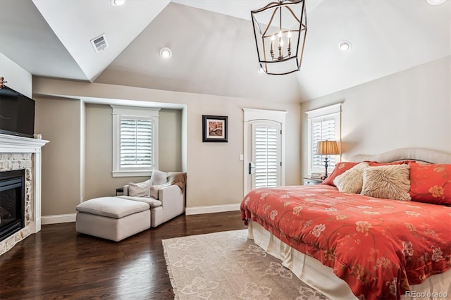 bedroom featuring vaulted ceiling, a stone fireplace, a notable chandelier, and dark hardwood / wood-style flooring