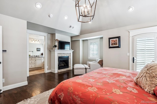 bedroom featuring dark hardwood / wood-style floors, connected bathroom, lofted ceiling, a tiled fireplace, and an inviting chandelier