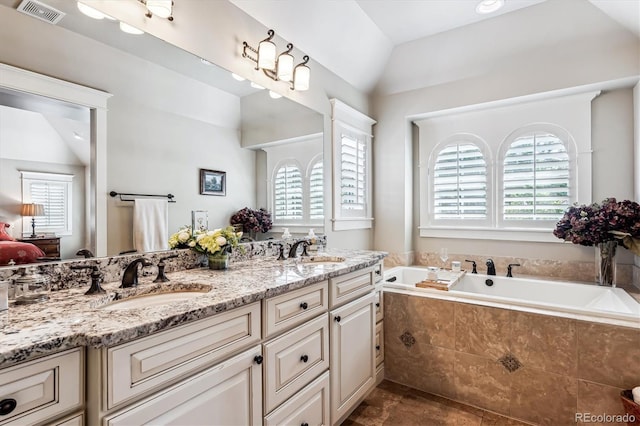 bathroom featuring lofted ceiling, vanity, and tiled tub