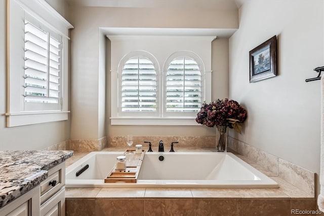 bathroom with tiled tub, vanity, and a healthy amount of sunlight