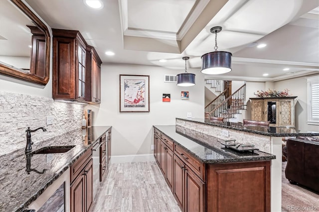 kitchen with sink, tasteful backsplash, ornamental molding, pendant lighting, and dark stone counters