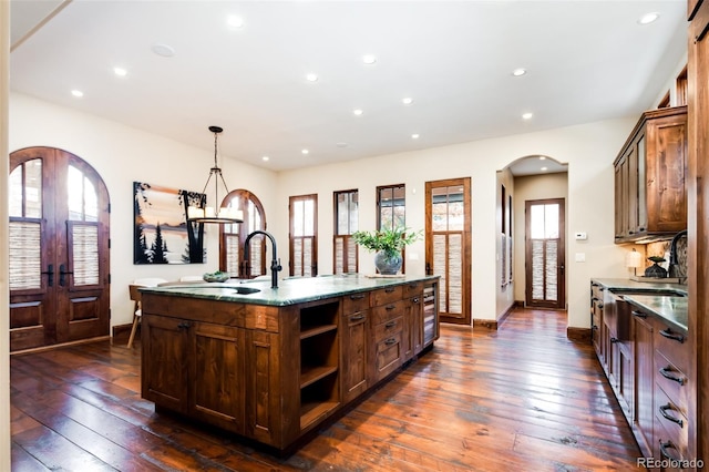 kitchen with dark wood-type flooring, a wealth of natural light, a center island with sink, and hanging light fixtures