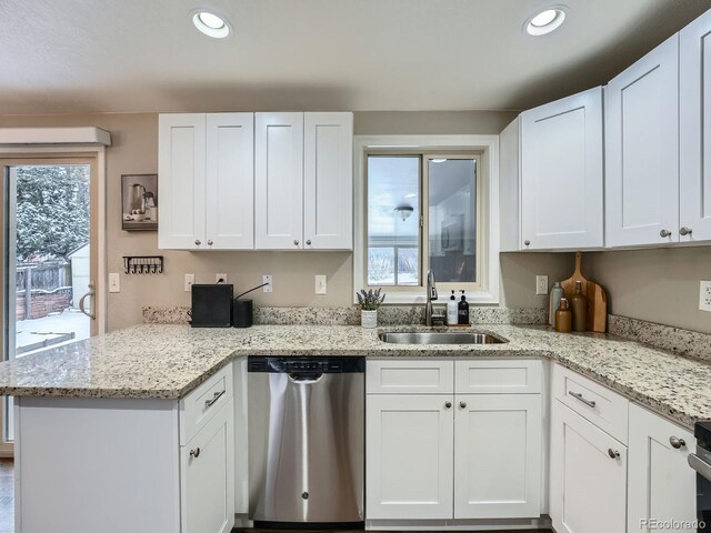 kitchen with kitchen peninsula, light stone counters, stainless steel dishwasher, sink, and white cabinets