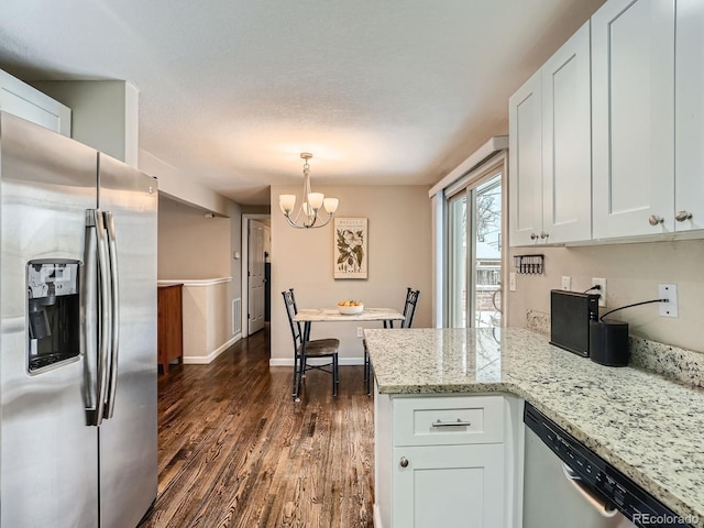 kitchen with light stone countertops, decorative light fixtures, white cabinetry, stainless steel appliances, and a chandelier