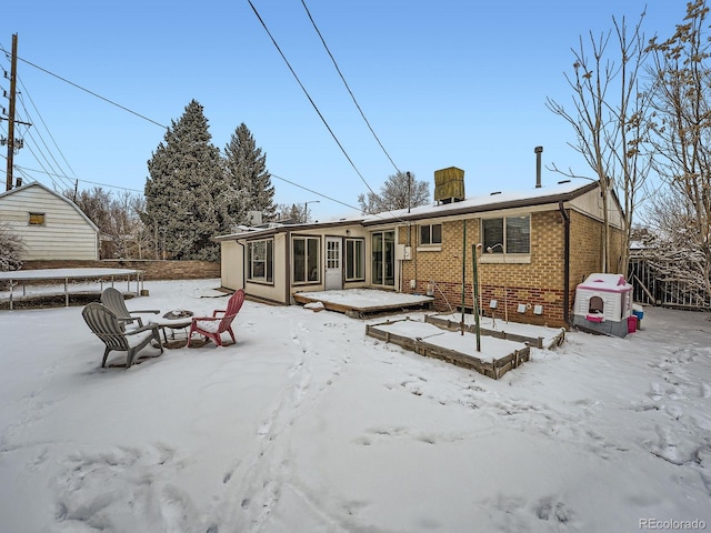 snow covered house with a sunroom, a fire pit, and a trampoline