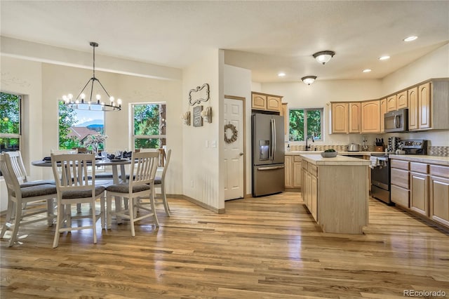 kitchen with hanging light fixtures, stainless steel appliances, light hardwood / wood-style floors, a kitchen island, and light brown cabinetry