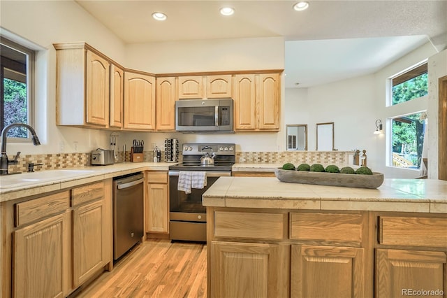 kitchen with light brown cabinetry, sink, light wood-type flooring, kitchen peninsula, and stainless steel appliances