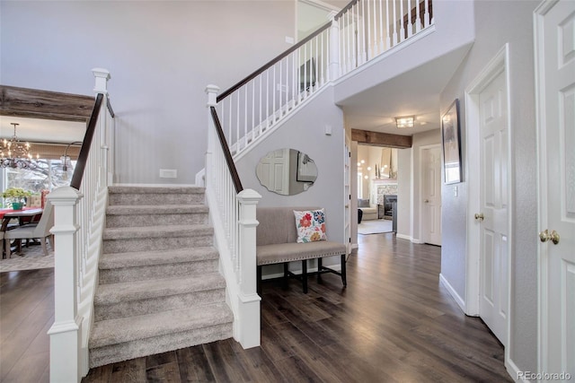 stairs with wood-type flooring, a stone fireplace, a notable chandelier, and a high ceiling