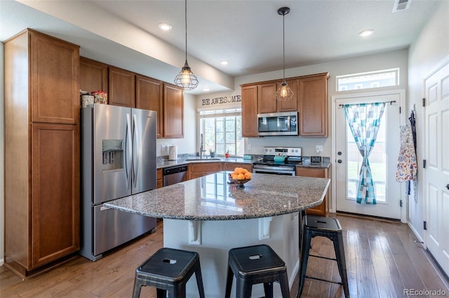 kitchen featuring dark stone counters, stainless steel appliances, brown cabinets, and a center island