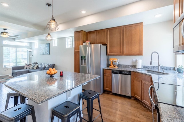 kitchen with appliances with stainless steel finishes, sink, light wood-type flooring, light stone countertops, and ceiling fan