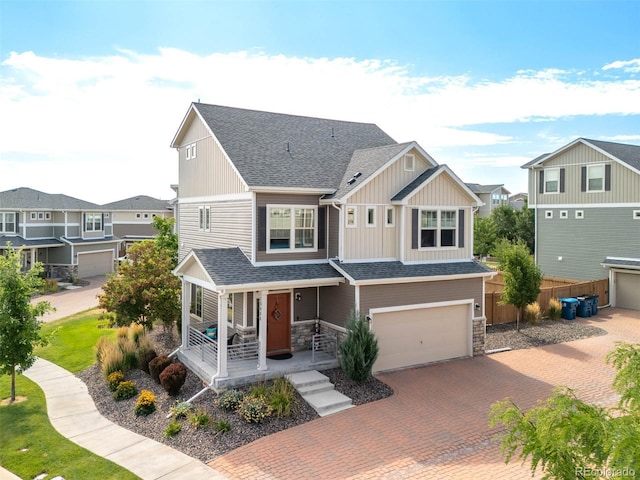 craftsman-style home with decorative driveway, a shingled roof, fence, a garage, and a residential view