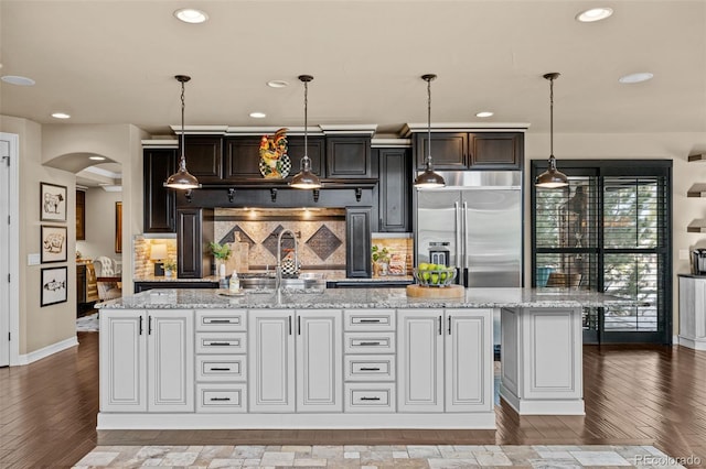 kitchen featuring decorative light fixtures, built in fridge, an island with sink, decorative backsplash, and white cabinets