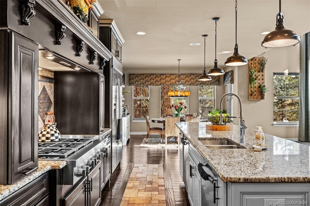 kitchen with a kitchen island with sink, sink, light stone counters, and decorative light fixtures