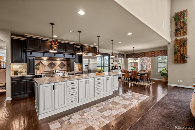 kitchen with built in refrigerator, decorative backsplash, white cabinets, and a spacious island