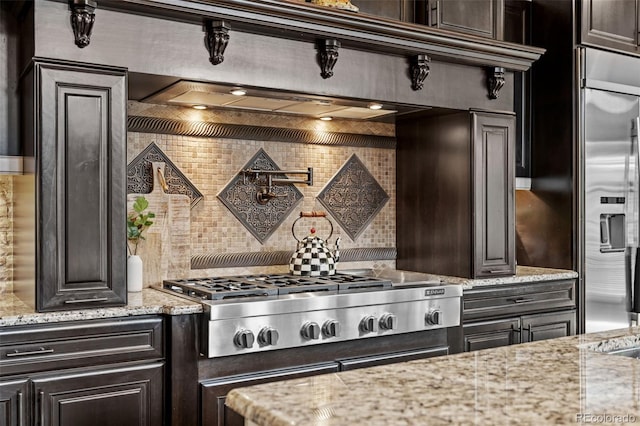 kitchen featuring light stone counters, dark brown cabinets, stainless steel appliances, and tasteful backsplash