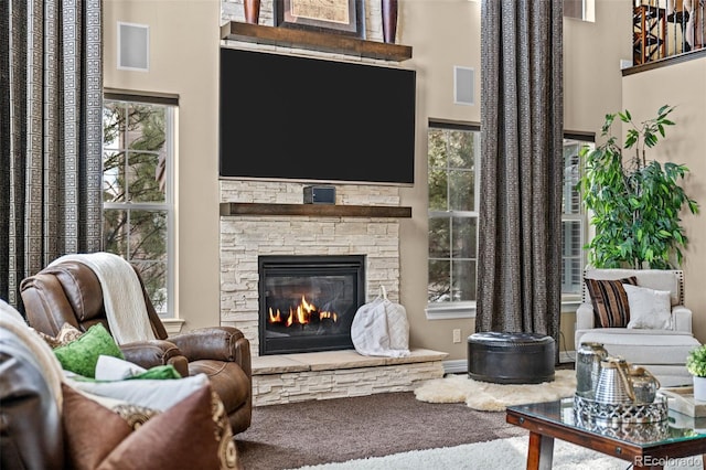 sitting room with a towering ceiling, a stone fireplace, carpet, and a wealth of natural light