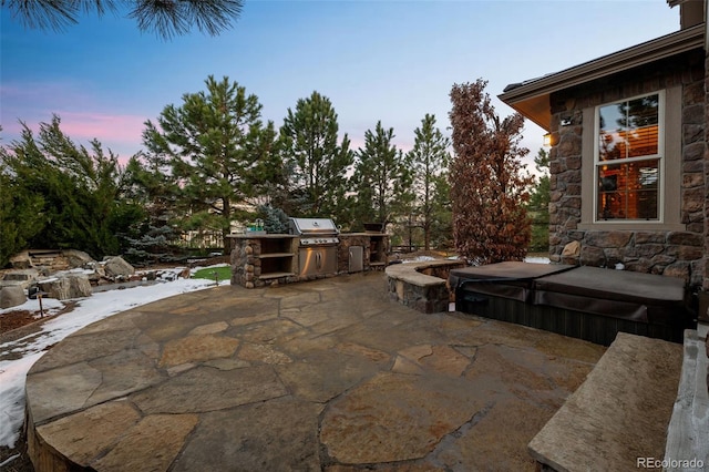 patio terrace at dusk with a grill, a covered hot tub, and an outdoor kitchen