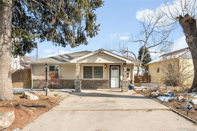 view of front of home with fence, stone siding, and stucco siding