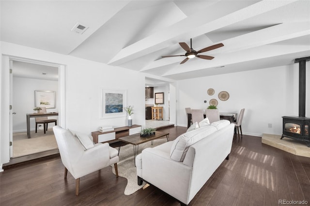 living area with lofted ceiling, a wood stove, dark wood-style floors, and visible vents