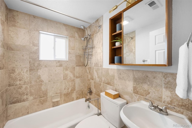 bathroom with visible vents, toilet, bathtub / shower combination, tile walls, and a sink