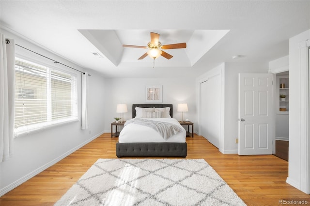 bedroom featuring light wood-style flooring, a raised ceiling, and baseboards