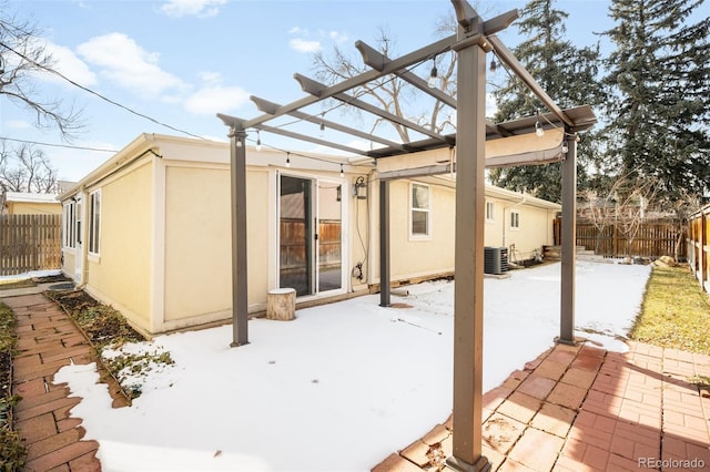 snow covered back of property featuring stucco siding, a pergola, fence, central AC unit, and a patio area