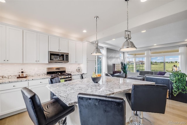 5280 Genoa St, Denver, CO 80249 - kitchen featuring appliances with stainless steel finishes, white cabinets, a breakfast bar, a kitchen island, and recessed lighting