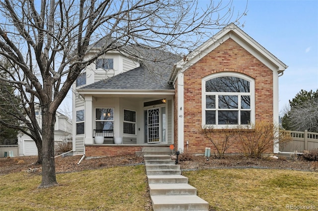 traditional-style home with a shingled roof, a front yard, and brick siding