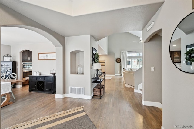 hallway featuring arched walkways, wood finished floors, visible vents, and baseboards