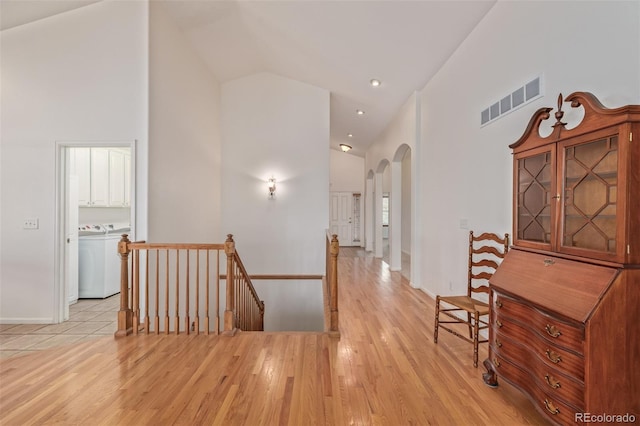 hall with visible vents, an upstairs landing, washer / dryer, arched walkways, and high vaulted ceiling