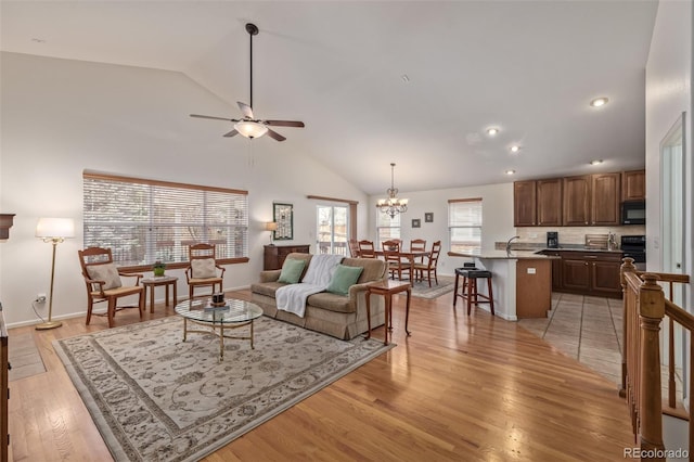 living room with ceiling fan with notable chandelier, light wood-style floors, baseboards, and high vaulted ceiling