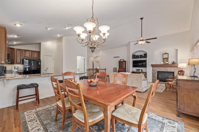 dining space featuring built in shelves, light wood-style flooring, a tiled fireplace, lofted ceiling, and ceiling fan