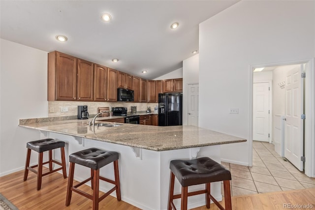 kitchen featuring a breakfast bar area, vaulted ceiling, a peninsula, black appliances, and a sink