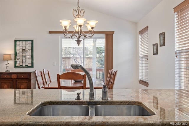 kitchen featuring light stone counters, a sink, hanging light fixtures, vaulted ceiling, and a chandelier