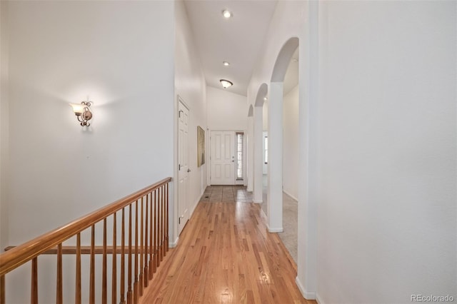 corridor with arched walkways, light wood-type flooring, and baseboards