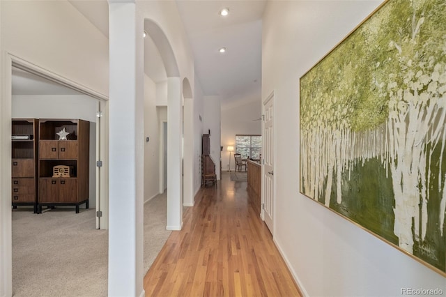 hall with recessed lighting, arched walkways, a high ceiling, light wood finished floors, and baseboards