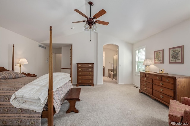 bedroom with visible vents, ensuite bath, arched walkways, light colored carpet, and vaulted ceiling