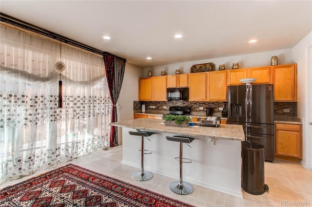 kitchen with light stone countertops, backsplash, black appliances, and a center island