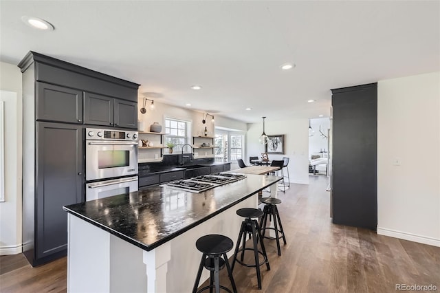 kitchen featuring open shelves, a sink, a kitchen breakfast bar, dark wood finished floors, and stainless steel appliances