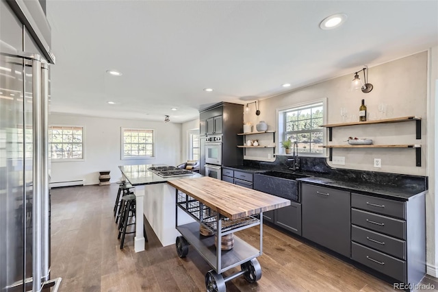 kitchen featuring open shelves, a baseboard radiator, appliances with stainless steel finishes, and wood finished floors