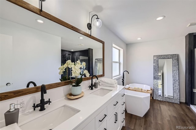 full bath featuring double vanity, a sink, a freestanding tub, and wood finished floors
