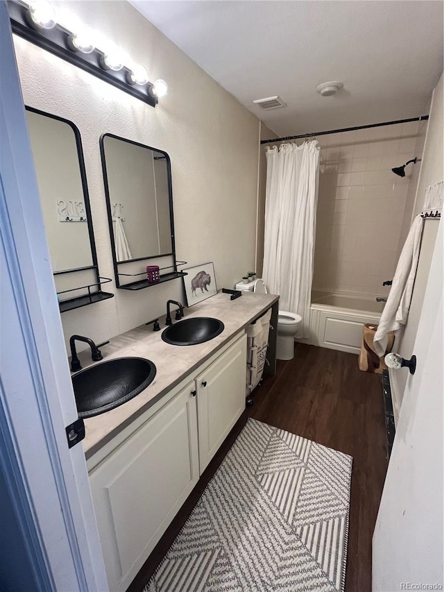 full bath featuring toilet, visible vents, a sink, and wood finished floors