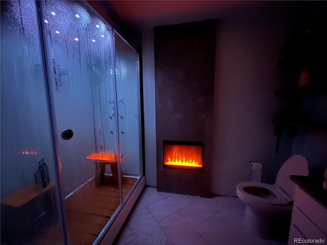 bathroom with toilet, a lit fireplace, and a stall shower
