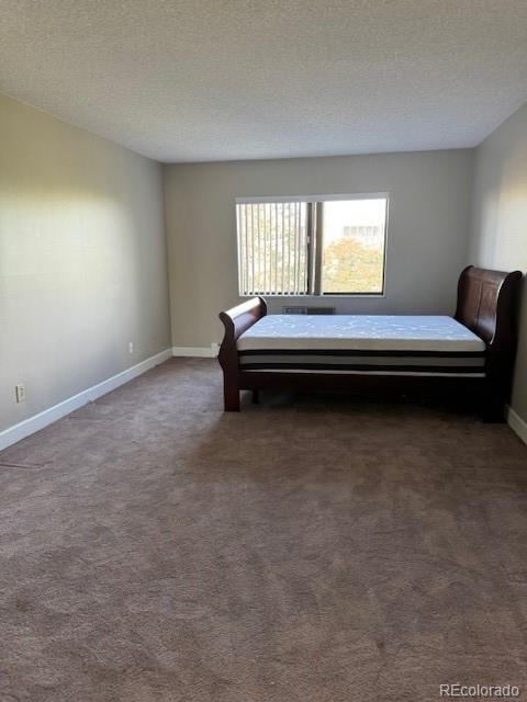 unfurnished bedroom featuring a textured ceiling and dark carpet