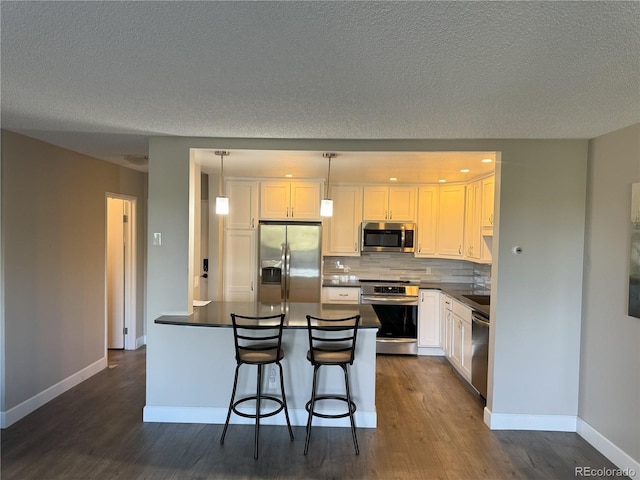 kitchen with appliances with stainless steel finishes, dark countertops, dark wood finished floors, white cabinets, and a textured ceiling
