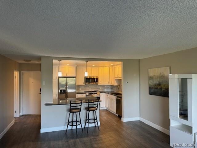 kitchen featuring stainless steel appliances, dark countertops, dark wood finished floors, a textured ceiling, and baseboards