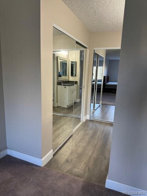 corridor featuring a textured ceiling, baseboards, and wood finished floors