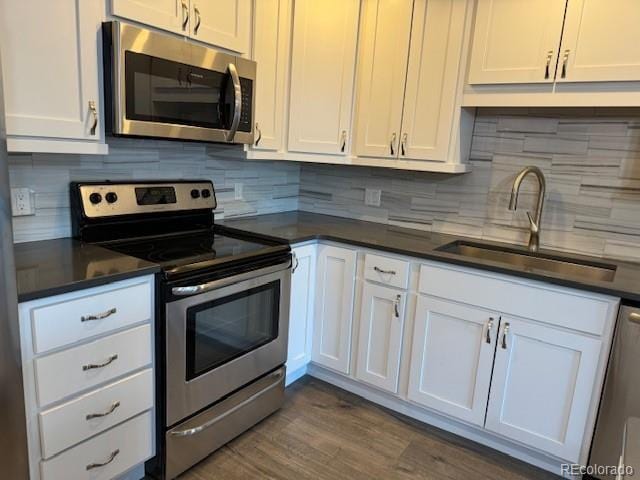 kitchen featuring stainless steel appliances, a sink, white cabinets, dark countertops, and tasteful backsplash