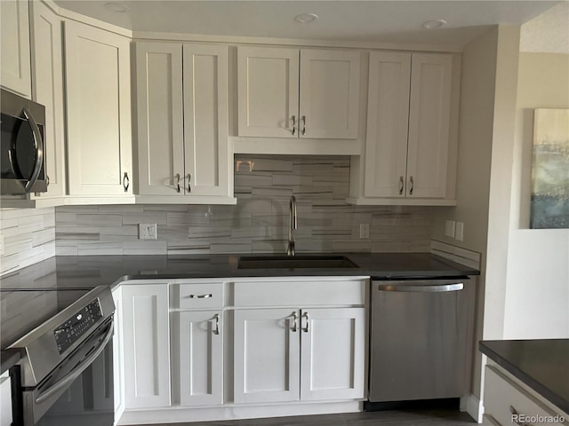 kitchen with stainless steel appliances, a sink, dark countertops, backsplash, and white cabinets
